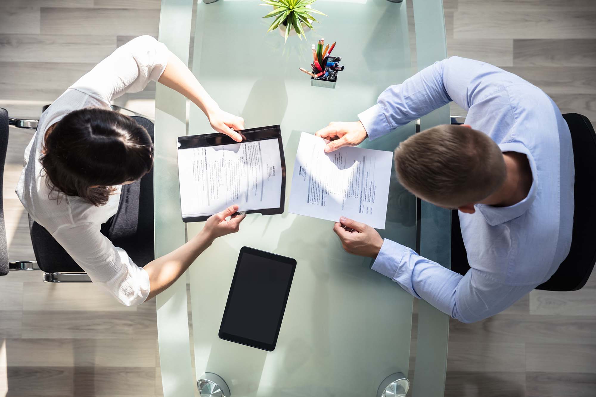 Elevated View Of Two Businesspeople Holding Resume Over Desk In Office